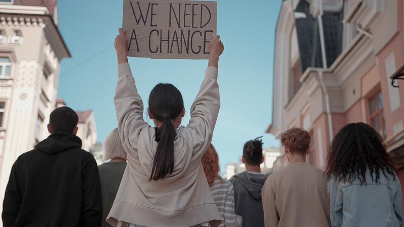 Frau Hält bei einer Demonstration ein Schild mit der Aufschrift "We need Change" hoch